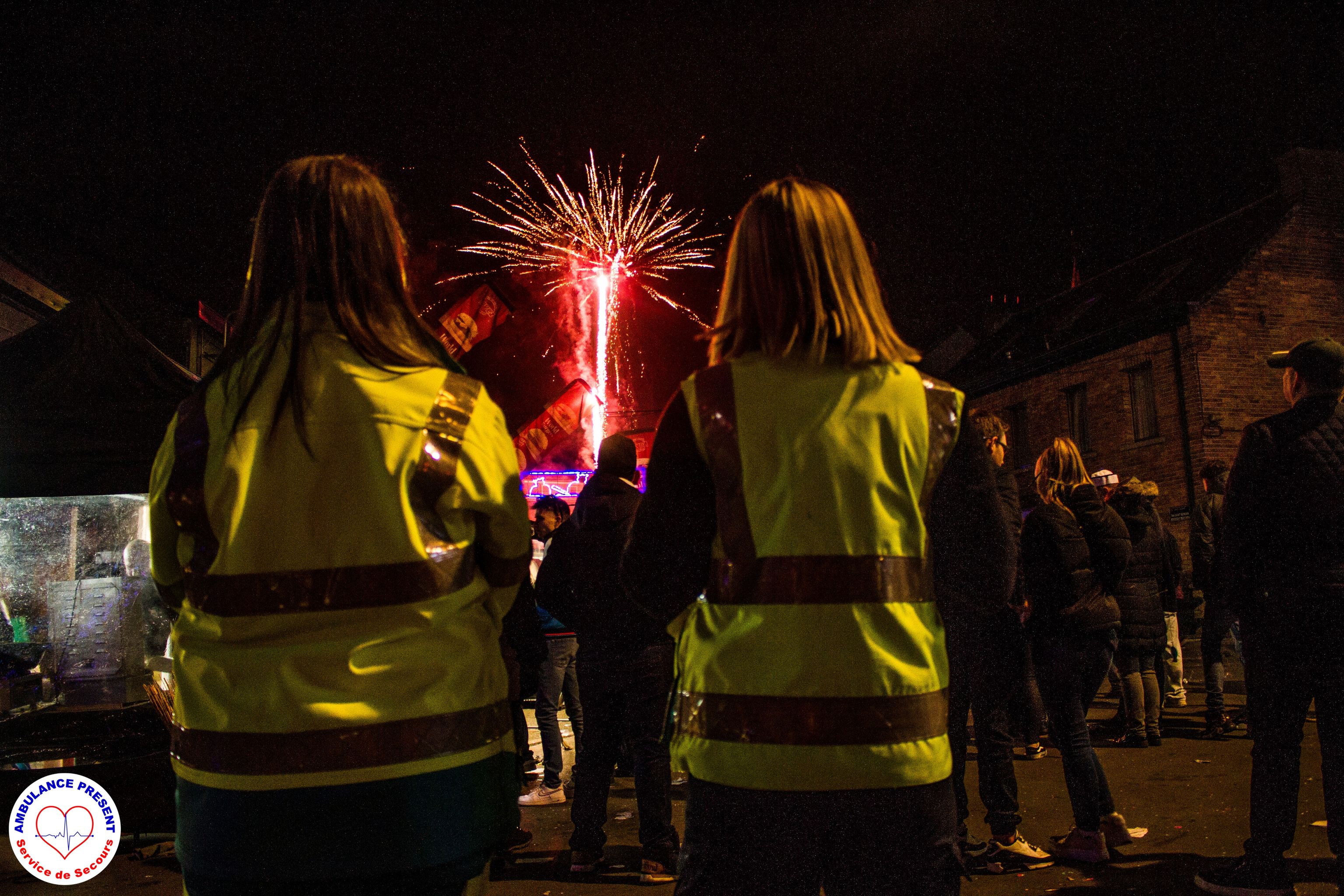 Deux secouristes en gilet jaune de dos devant un feu d'artifice